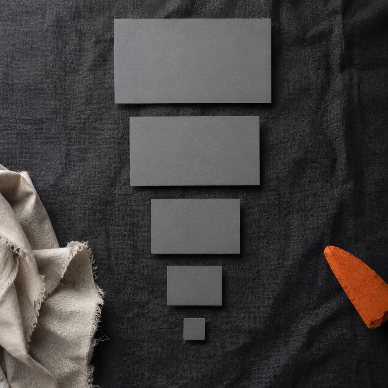 Five plain grey rectangles of decreasing size on near-black cloth, the smallest almost lost in the texture.