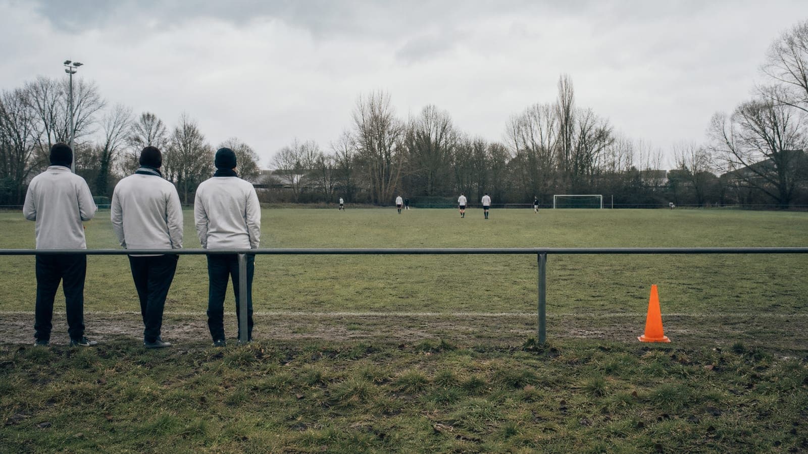 An empty amateur sports pitch seen from the touchline with distant figures in plain training tops.
